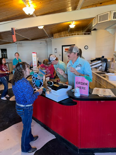 A women in a blue shirt places her ice cream order at the Eddy County Extension Office at the station that says "Order Here" on a bright pint sign. The individual taking the order is in a denim shirt and denim hat. 