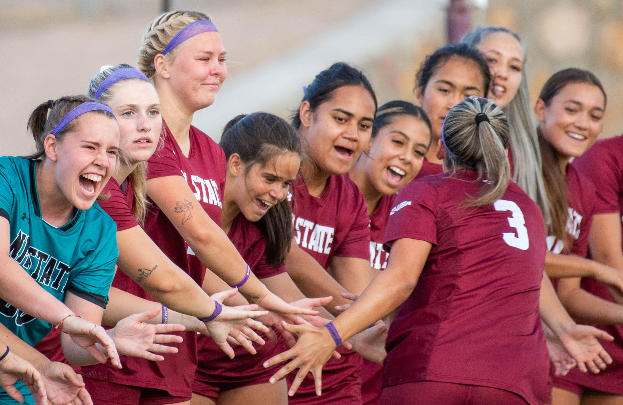 Members of the NMSU Women's soccer team line up to give high fives to a member running down the line. 
