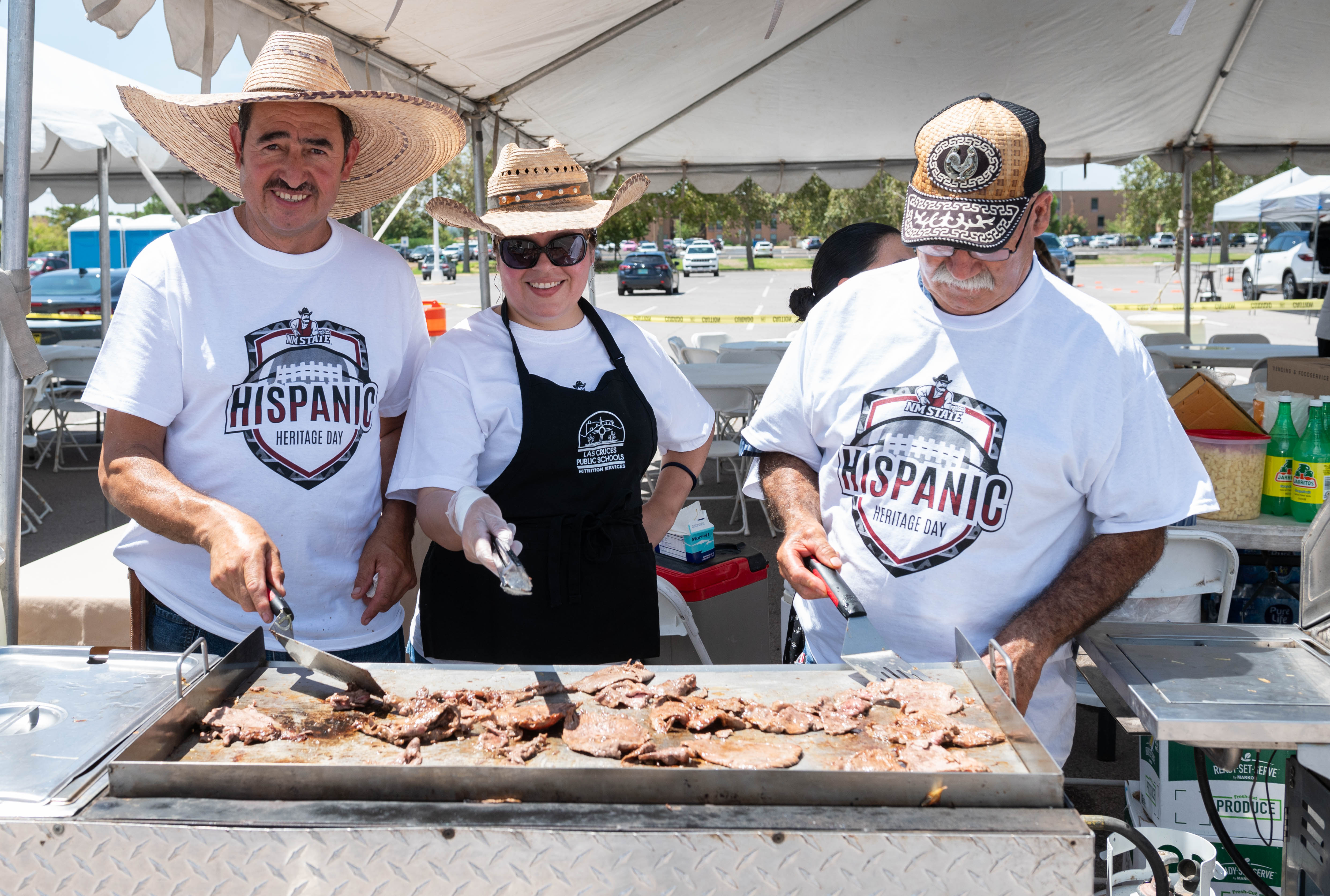 Three individuals stand in front of a flat top grill cooking during the hispanic heritage football game on August 26, 2023. (New Mexico State University's Home Football opener against University of Massacusetts. (NMSU photo by Josh Bachman))