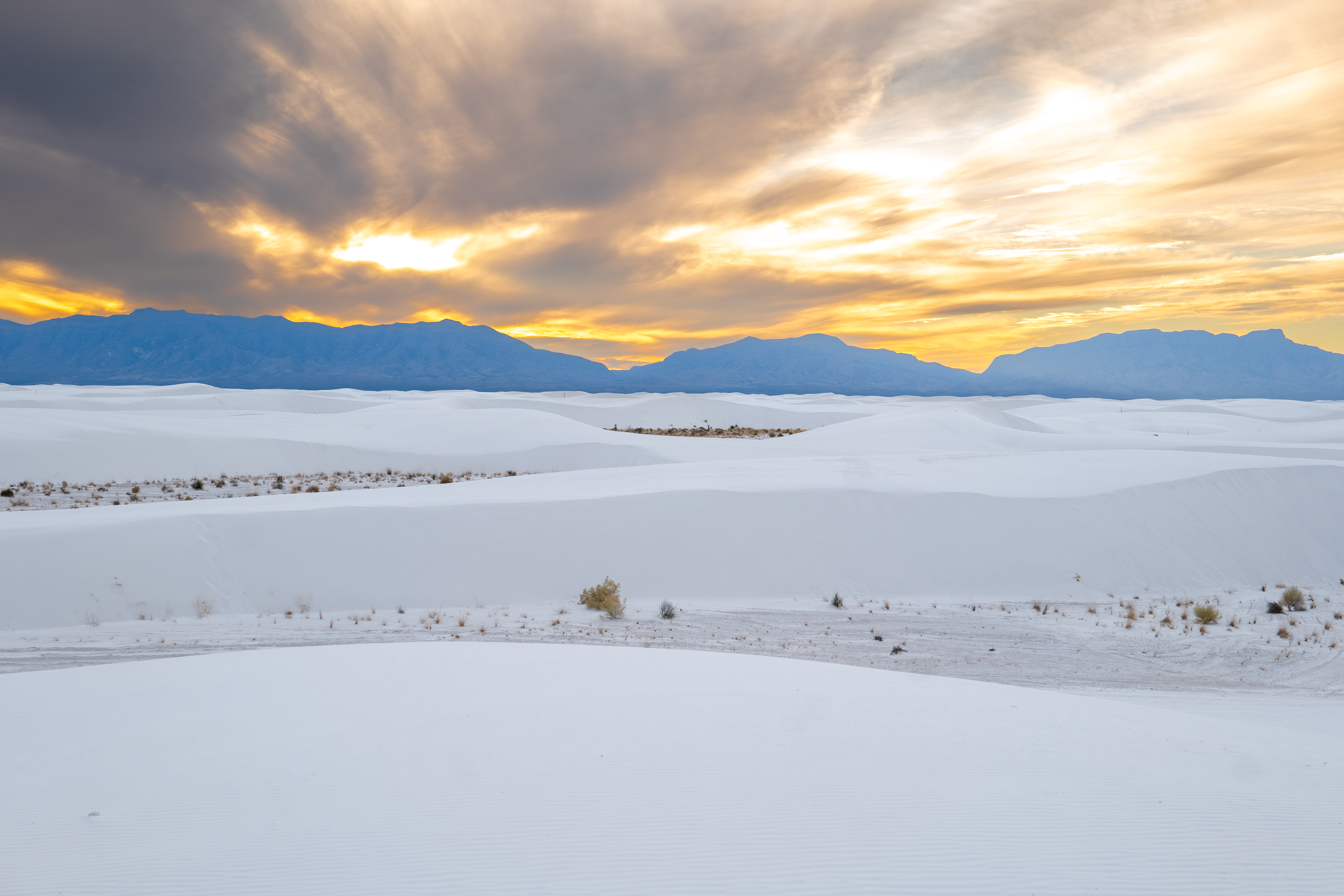 Landscape photo of White Sands National Park during sunset with the sun setting behind the mountains. 