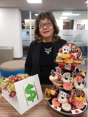 Gloria Podruchny stands behind a casino themed tower of mini doughnuts and a box of flowers with a large green dollar sign on the front. 