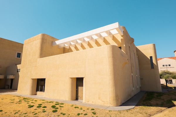 Modern beige stucco building with a white overhang and small windows under a clear blue sky.