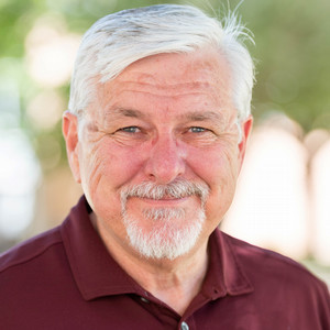 Headshot of Dr. Chris Erickson - A smiling older man with gray hair and a beard, wearing a maroon polo shirt.